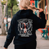 Person wearing a black hoodie with 'Thirsty Girl Social Club' design on the back, walking outdoors.