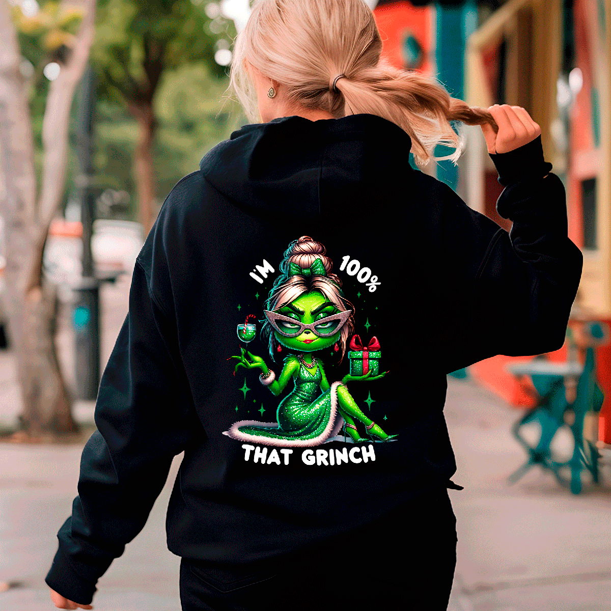 Person wearing a black hoodie with a green character design and text on the back, walking outdoors.