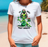 Person wearing a white t-shirt with a green character design and text on a beach.