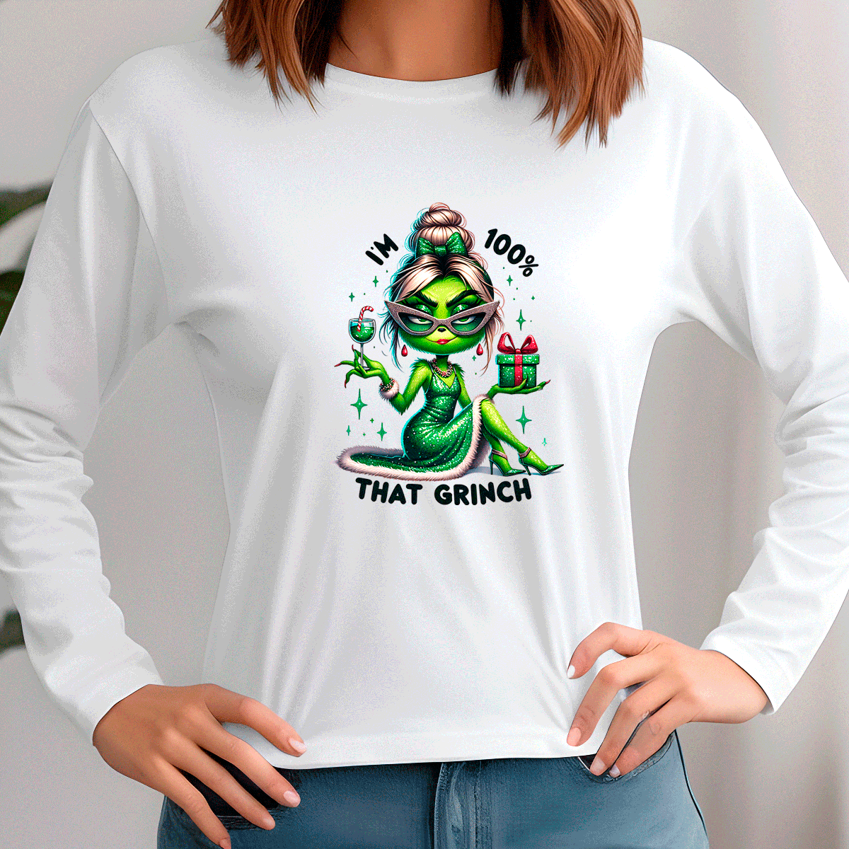 White long-sleeve shirt with a graphic design of a green character holding a gift and text 'IM 100% THAT GRINCH' worn by a person.
