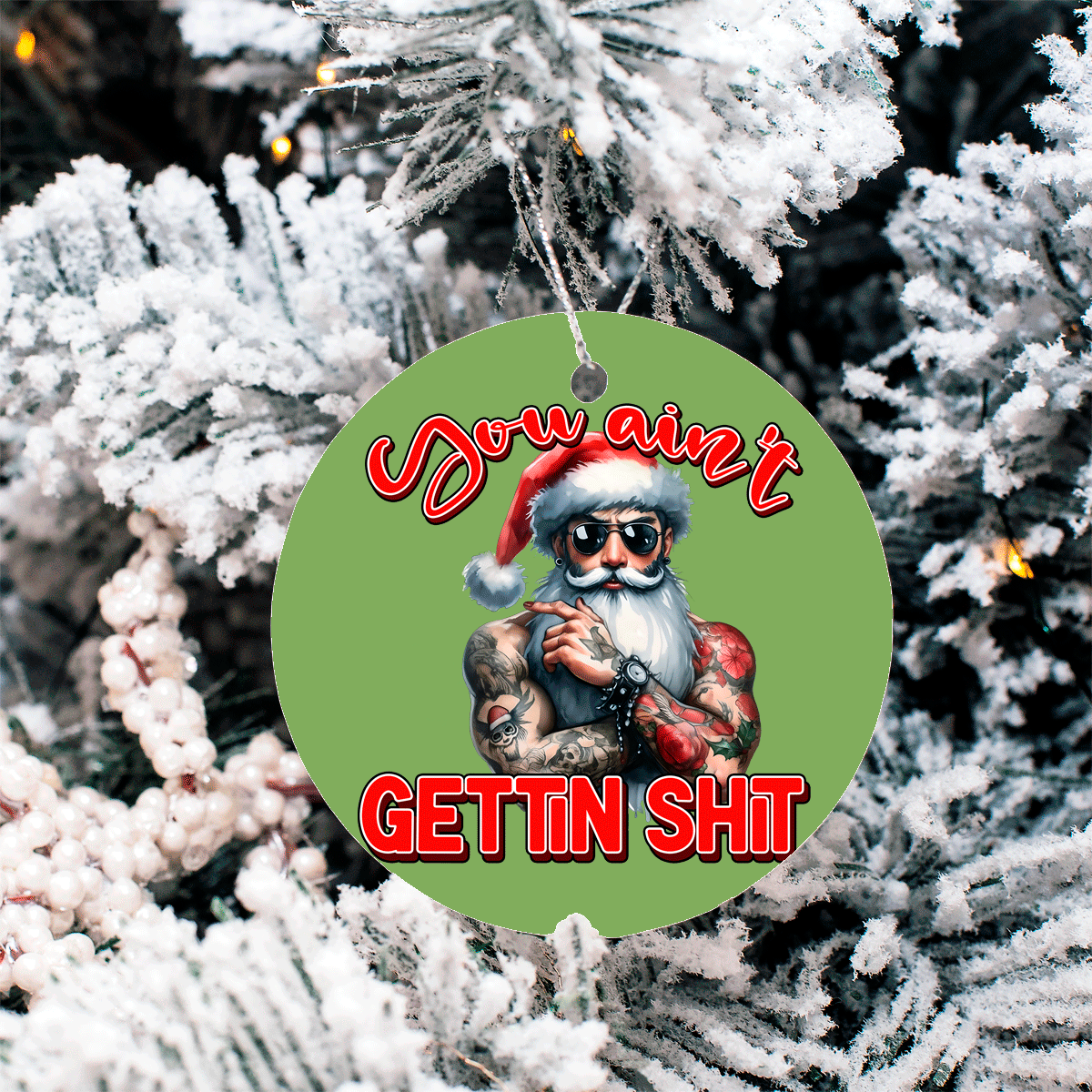 Decorative ornament with a tattooed Santa Claus design on a green background, hanging against a snowy tree.
