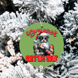 Decorative ornament with a tattooed Santa Claus design on a green background, hanging against a snowy tree.