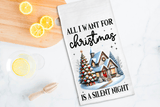 Tea towel with Christmas design and text on a kitchen counter with lemons and a wooden spoon.