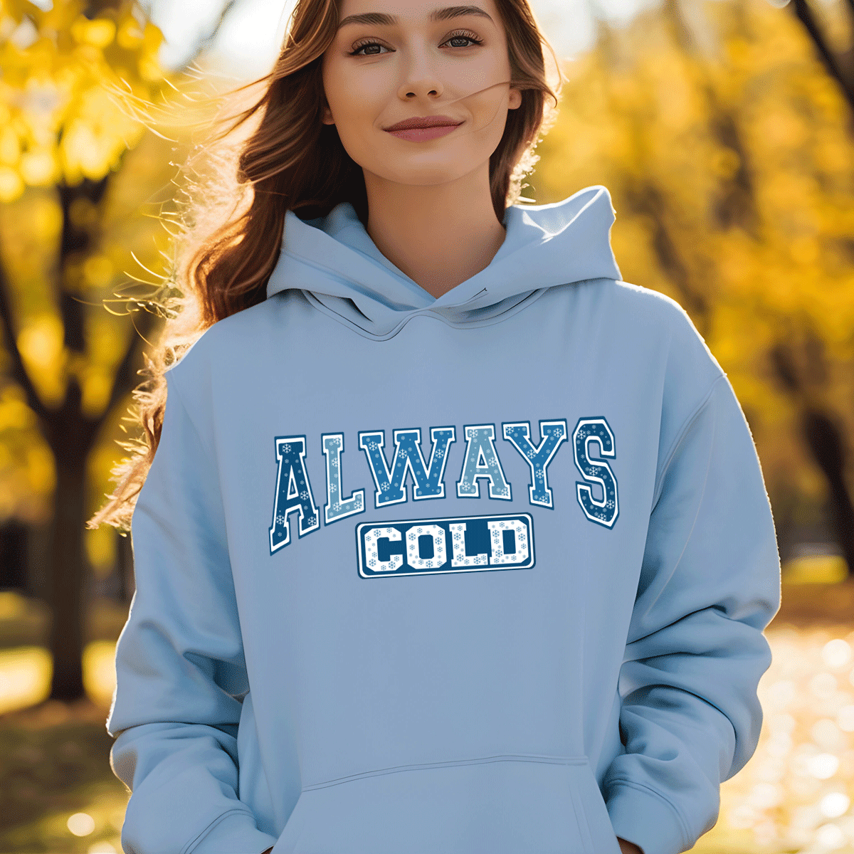Person wearing a light blue hoodie with 'ALWAYS COLD' text in an outdoor setting with trees.