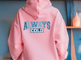 Pink hoodie with 'ALWAYS COLD' text on a blue wall background