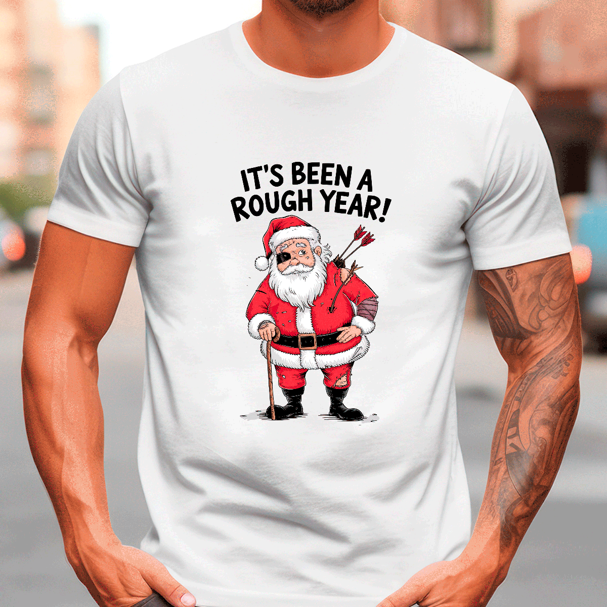White t-shirt with a graphic of Santa Claus holding an axe and text 'It's Been a Rough Year!' on a blurred street background.