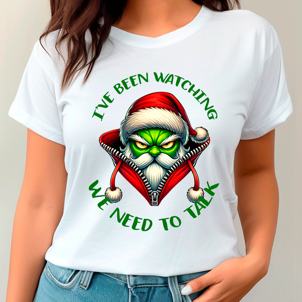 White t-shirt with a graphic design of a character in a Santa hat with text 'I've been watching. We need to talk.'