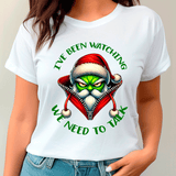 White t-shirt with a graphic design of a character in a Santa hat with text 'I've been watching. We need to talk.'