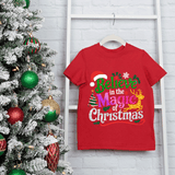 Red t-shirt with Christmas-themed text next to a decorated Christmas tree on a light gray wooden background