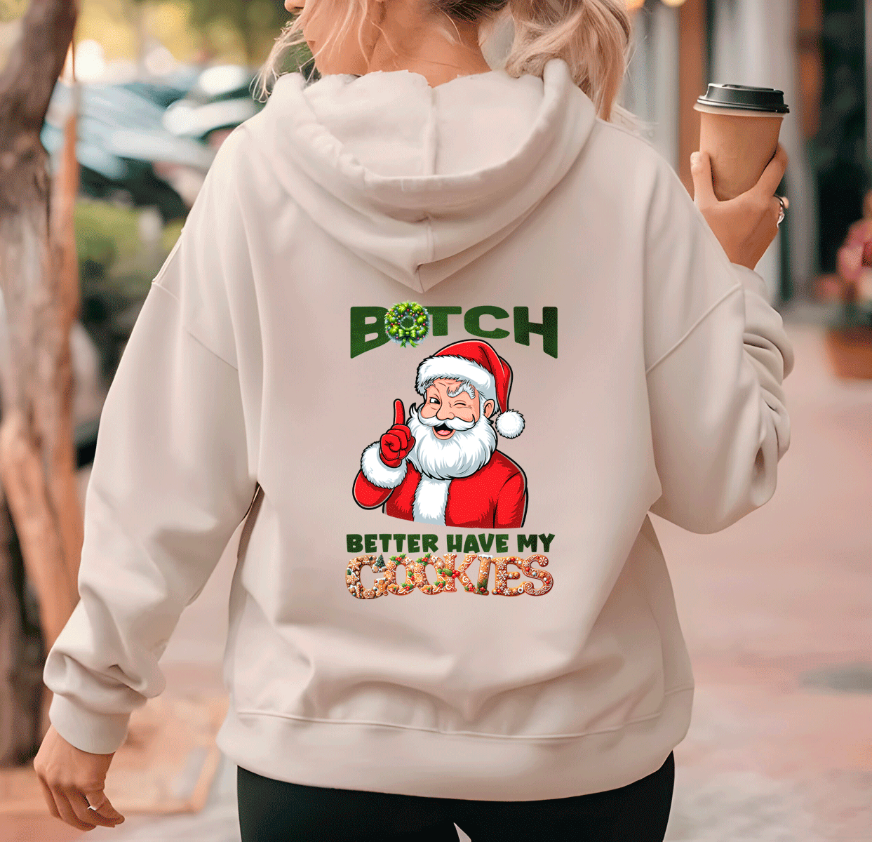 Person wearing a hoodie with a graphic of Santa Claus and text, holding a coffee cup.