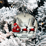 Christmas ornament with reindeer and sleigh design hanging on a snow-covered tree.