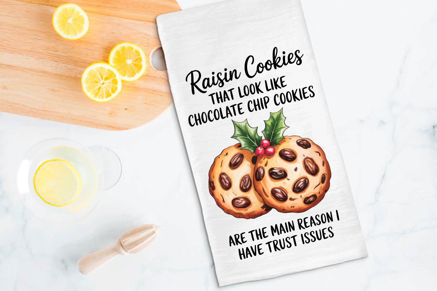 Tea towel with raisin cookies illustration and humorous text on a kitchen counter with lemons.