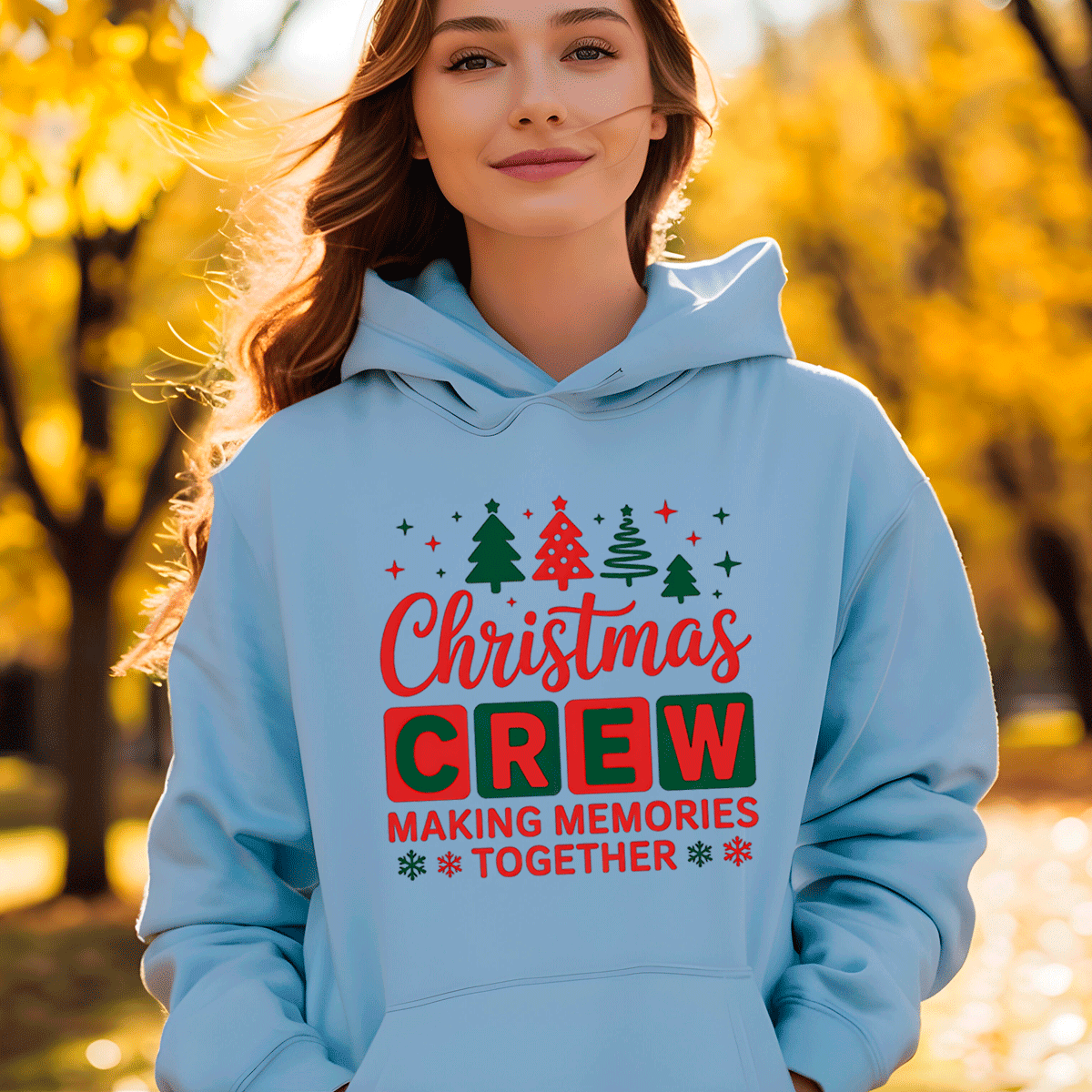 Person wearing a light blue hoodie with Christmas-themed text in an outdoor setting with trees.