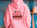 Pink hoodie with Christmas-themed text on a blue wall background