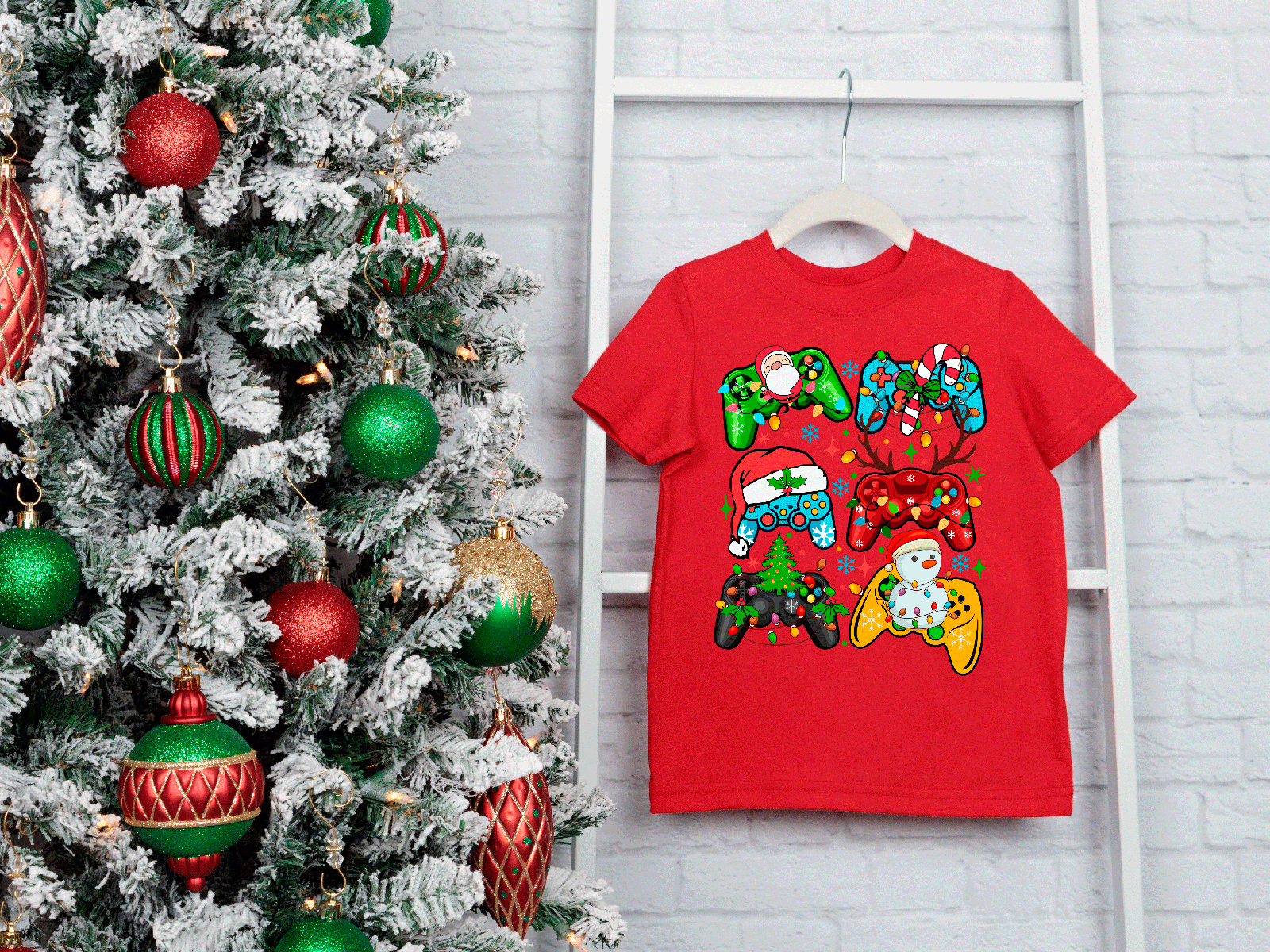 Red t-shirt with Christmas-themed design next to a decorated Christmas tree on a white brick wall.