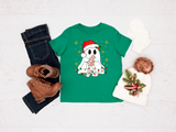 Green t-shirt with a ghost wearing a Santa hat and Christmas lights design, paired with jeans, boots, and a decorative bag on a light background.