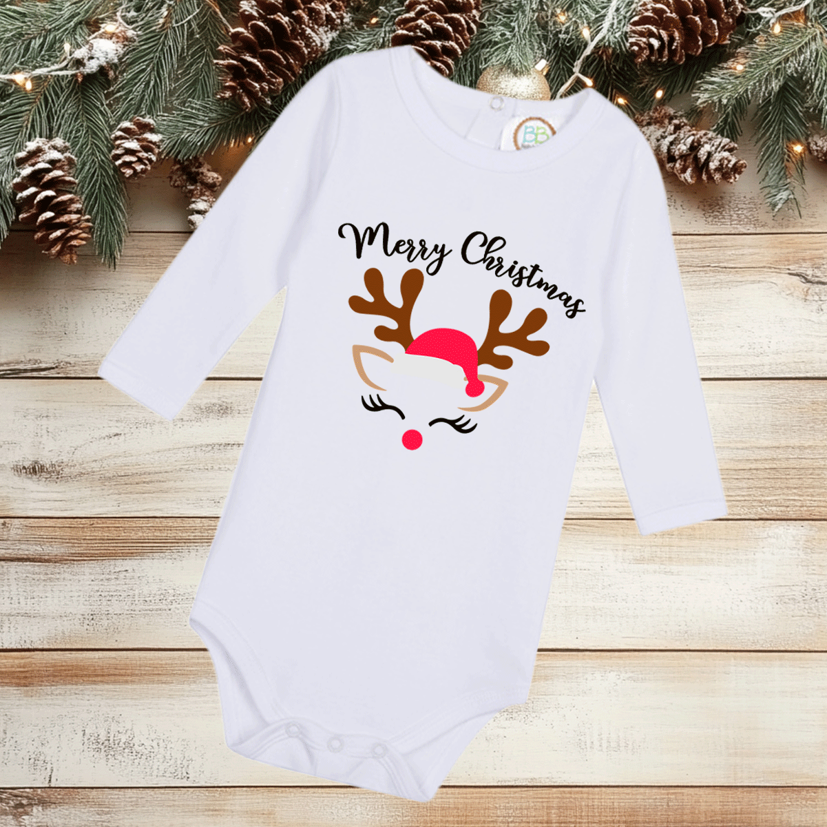 White baby onesie with Christmas design on a wooden surface with pine branches and pinecones.