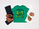 Green t-shirt with Christmas wreath design and text, paired with jeans, boots, and a hat on a light background.