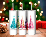 Three white tumblers with Christmas tree designs on a wooden surface with blurred lights and presents in the background.