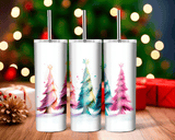 Three white tumblers with Christmas tree designs on a wooden surface with blurred lights and presents in the background.