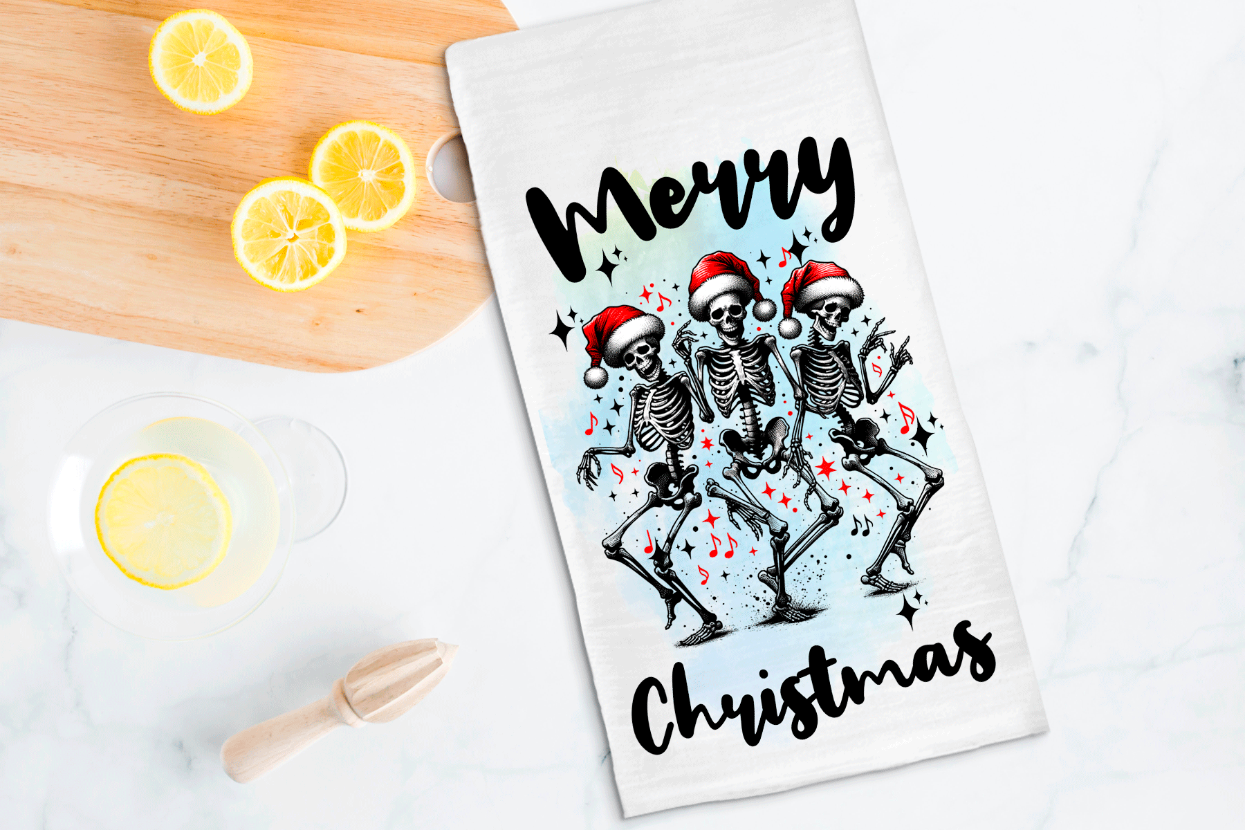 Tea towel with skeletons wearing Santa hats and 'Merry Christmas' text on a kitchen counter with lemons.