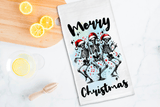 Tea towel with skeletons wearing Santa hats and 'Merry Christmas' text on a kitchen counter with lemons.