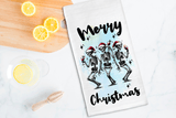Tea towel with skeletons and 'Merry Christmas' text on a kitchen counter with lemons.