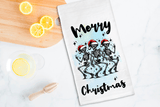 Tea towel with skeletons wearing Santa hats and 'Merry Christmas' text on a kitchen counter with lemons.