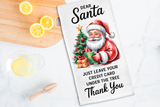 Tea towel with Santa Claus design and humorous text on a kitchen counter with lemons.