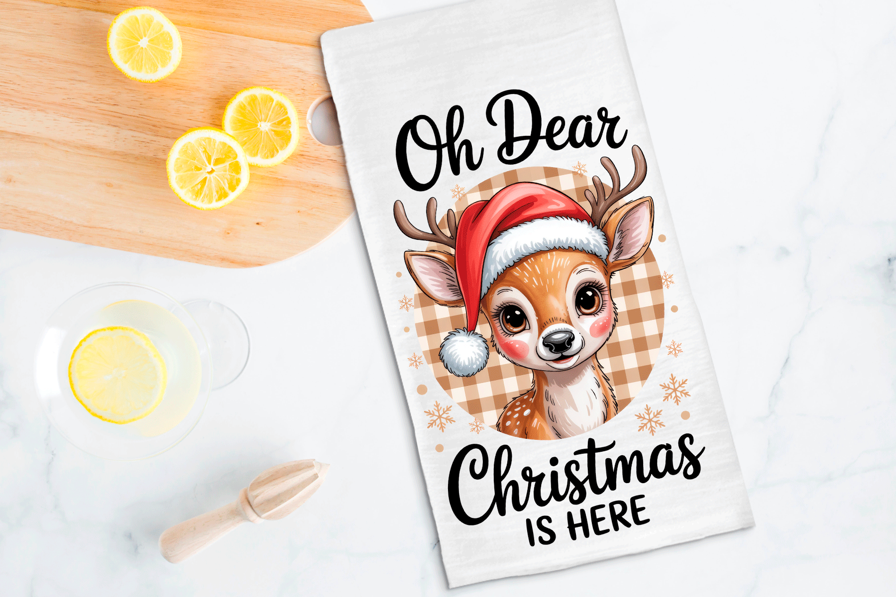 Tea towel with a Christmas-themed design of a deer wearing a Santa hat, text 'Oh Dear Christmas is Here', on a wooden surface with lemons.