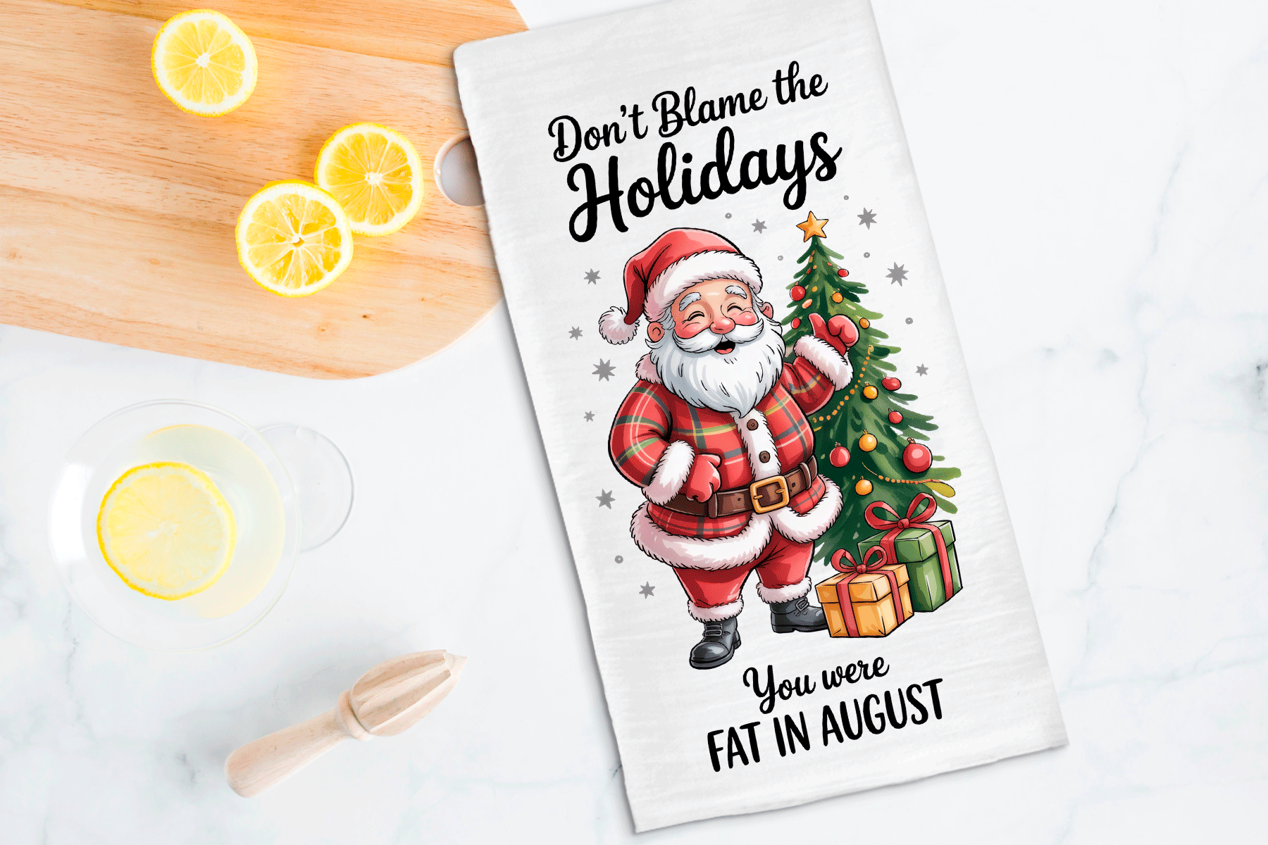 Tea towel with Santa Claus design and humorous text on a kitchen counter with lemons and a cutting board.