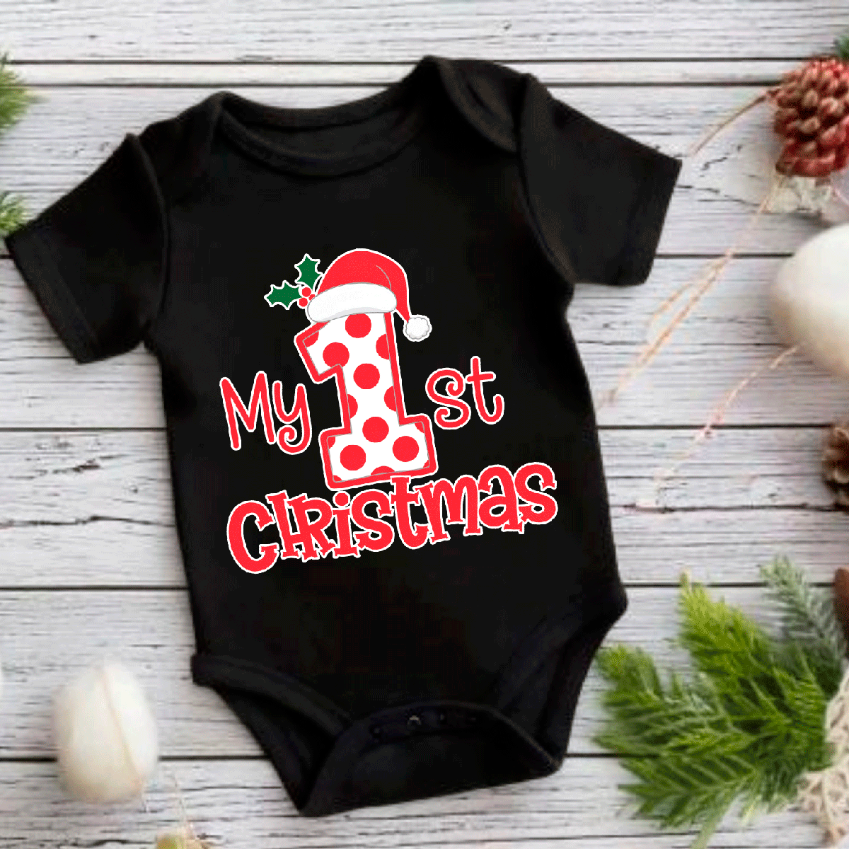 Black baby onesie with 'My 1st Christmas' print featuring a Santa hat on a wooden surface with Christmas decorations.