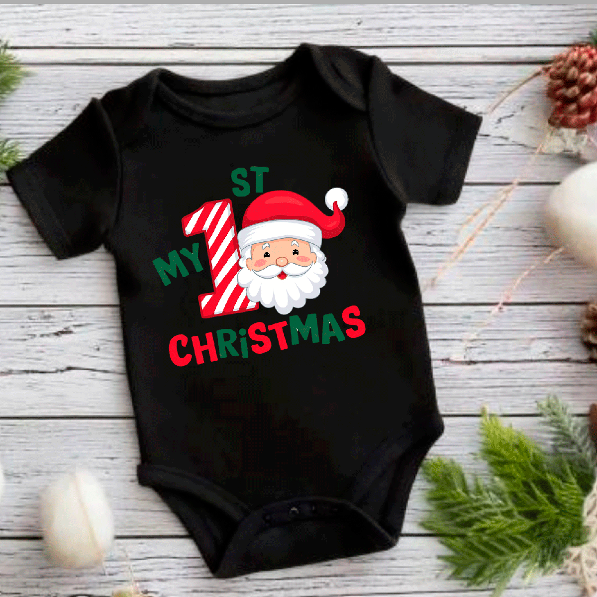Black baby onesie with Santa Claus design and text on a wooden surface with Christmas decorations.
