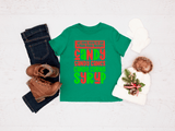 Green t-shirt with colorful text, jeans, boots, and a decorative item on a light background