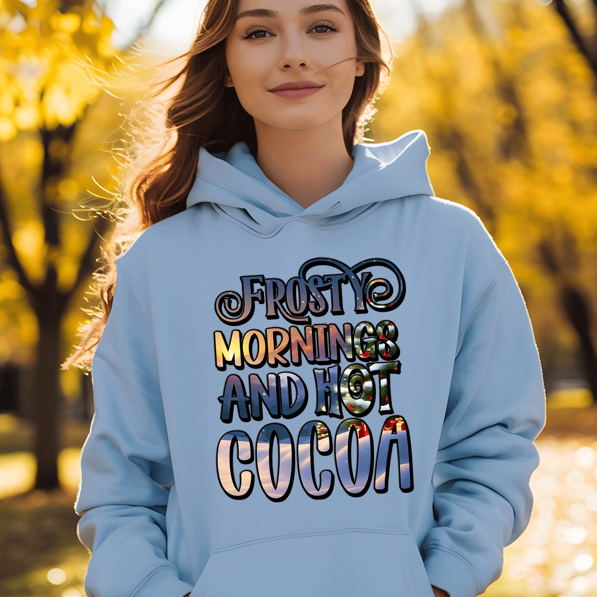 Person wearing a light blue hoodie with 'Frosty Mornings and Hot Cocoa' text in an autumn setting.