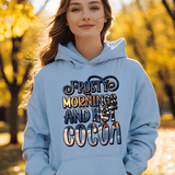 Person wearing a light blue hoodie with 'Frosty Mornings and Hot Cocoa' text in an autumn setting.