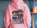 Pink hoodie with colorful text 'Frosty mornings and hot cocoa' on a blue wall background.