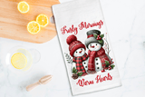 Tea towel with snowman design and text on a kitchen counter with lemons.