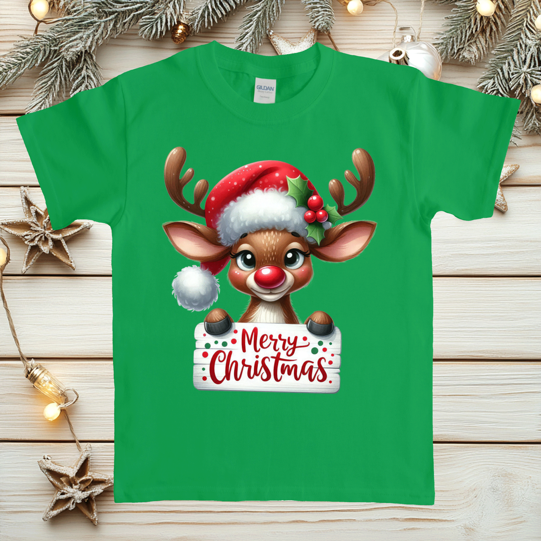 Green t-shirt with a reindeer holding a 'Merry Christmas' sign on a wooden surface with Christmas decorations.