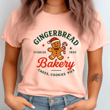 Person wearing a pink t-shirt with a gingerbread-themed design on a plain background