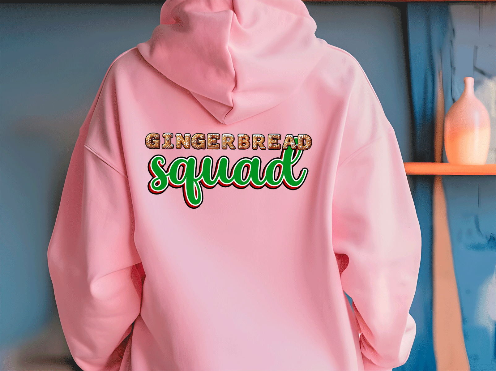 Pink hoodie with 'Gingerbread Squad' text on the back against a blue wall.