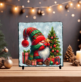 Decorative Christmas slate with a gnome and tree on a wooden surface with festive decorations.