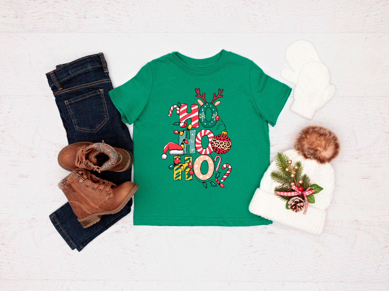 Green t-shirt with Christmas design, jeans, boots, and a hat on a light background