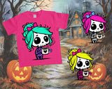 Pink t-shirt with cartoon skeleton design featuring colorful hair and a cup, set against a Halloween-themed background with pumpkins and a house.