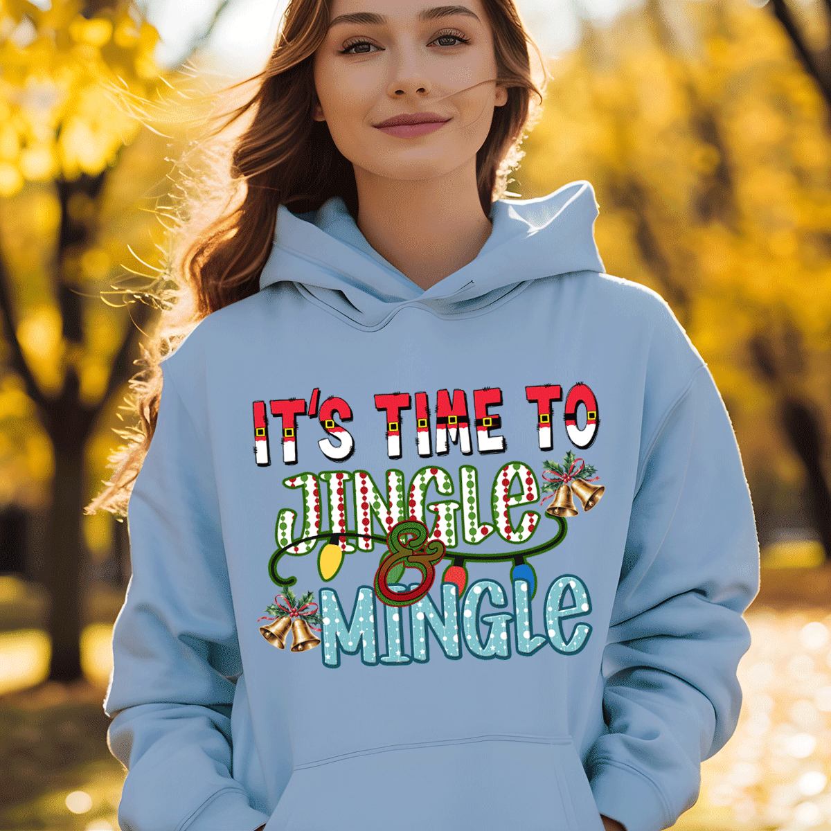 Person wearing a light blue hoodie with 'It's Time to Jingle & Mingle' text in an autumn setting