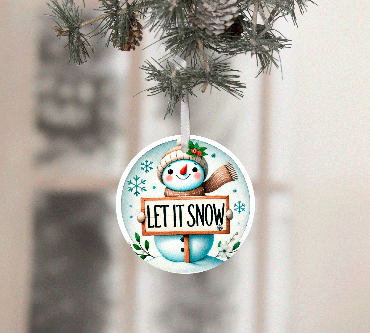 Christmas ornament with snowman holding 'Let It Snow' sign, hanging on a tree.