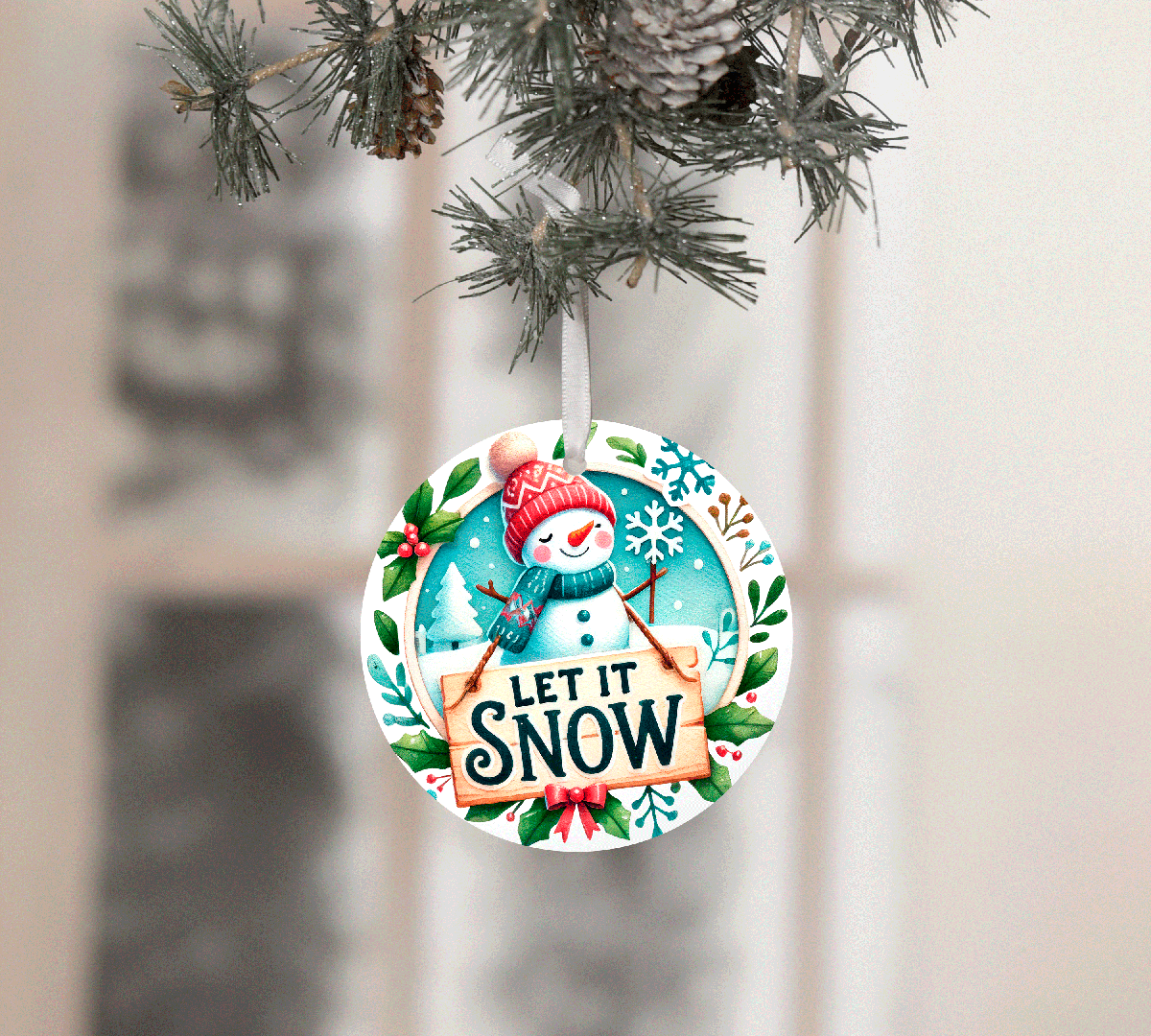 Christmas ornament with snowman design and 'Let It Snow' text, hanging on a tree.