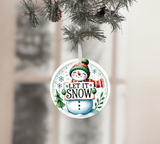 Christmas ornament with snowman design and 'Let It Snow' text, hanging on a tree.