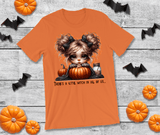 Orange t-shirt with a Halloween-themed design featuring a witch and pumpkins on a wooden surface with decorative items.