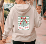Person wearing a hoodie with a Christmas design and text, holding a coffee cup.